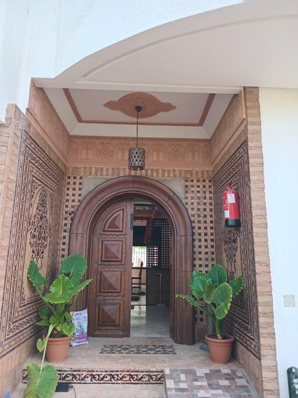 Entrée du centre de yoga Yoga You à Casablanca : porte en bois sculpté encadrée de zellige et de plâtre ciselé
