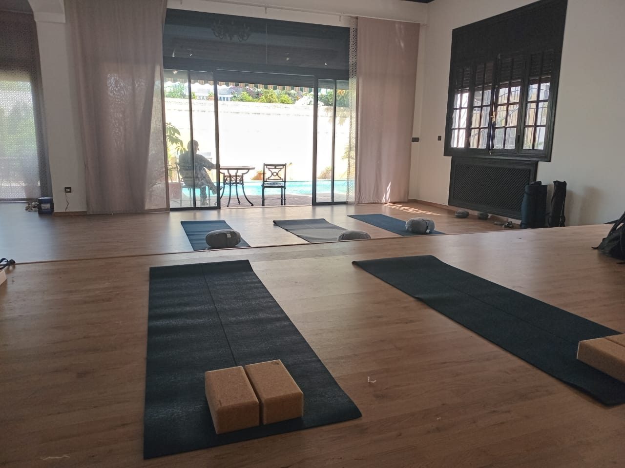Salle de yoga du centre Yoga You à Casablanca : tapis, briques et bolsters devant la baie vitrée ouverte sur le jardin